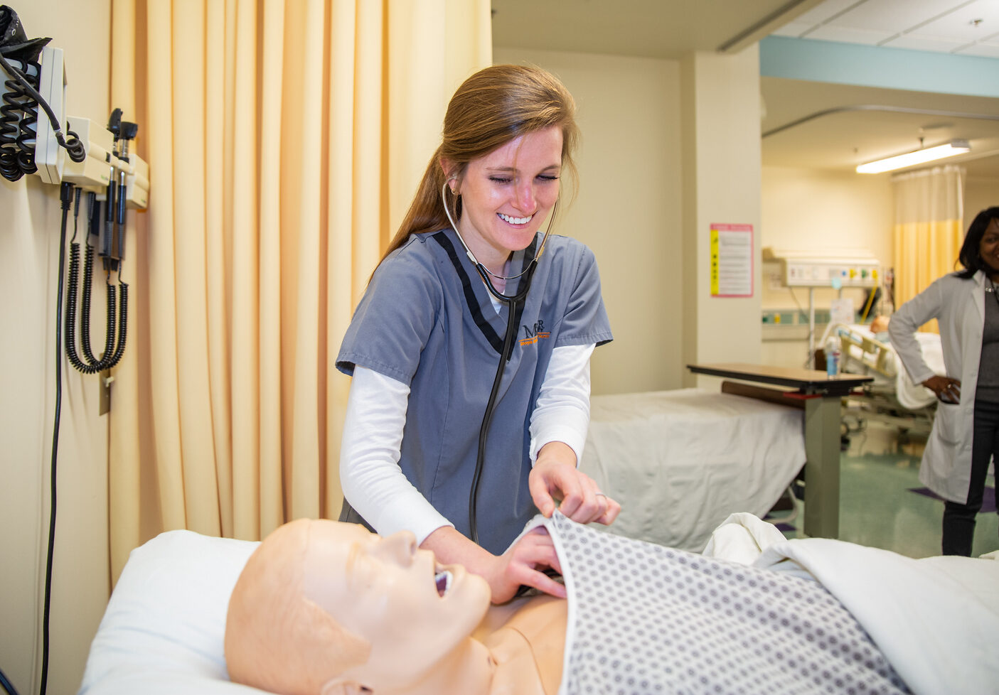 Mercer nursing student in scrubs, smiling and checking heartbeat of manikin in lab