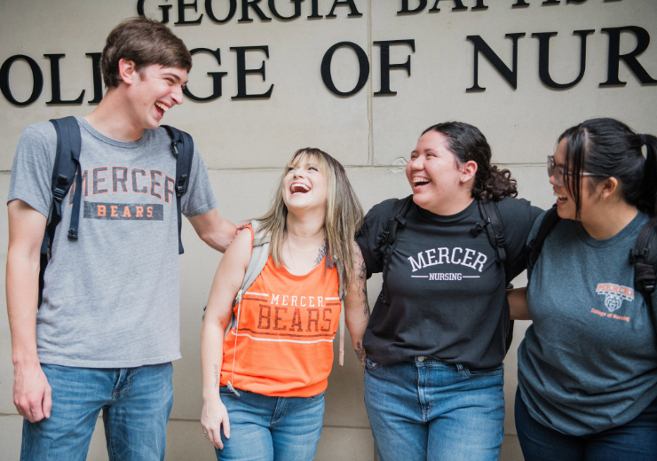 four students laughing and smiling in front of the nursing building