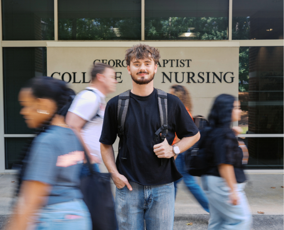 male student smiling at the camera with other students walking around him