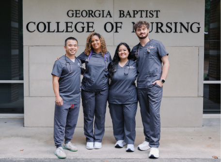 four nursing students in scrubs standing in front of the nursing building
